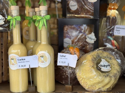 Bottles of Eierlikör, a vegan nut cake, and a loaf of bread with poppy seeds are displayed in a shop with price tags.