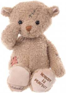 A fluffy teddy bear with a stitched patch on its head, patchwork on its leg, and "Nobody is Perfect" embroidered on its foot.