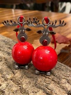 Two reindeer ornaments with red spherical bodies and metal antlers stand on a wooden surface, with a blurred background.