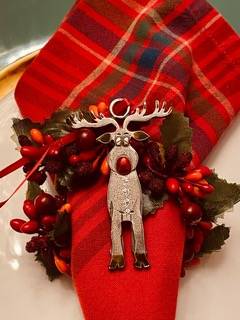 Festive napkin with a plaid pattern, adorned with a silver reindeer ring and red berries, set on a white plate.
