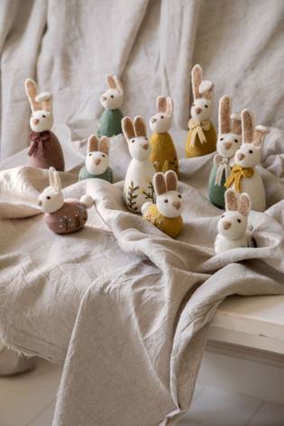 Felt bunny figures with colorful scarves and floral patterns on a beige cloth backdrop, arranged in a decorative display.
