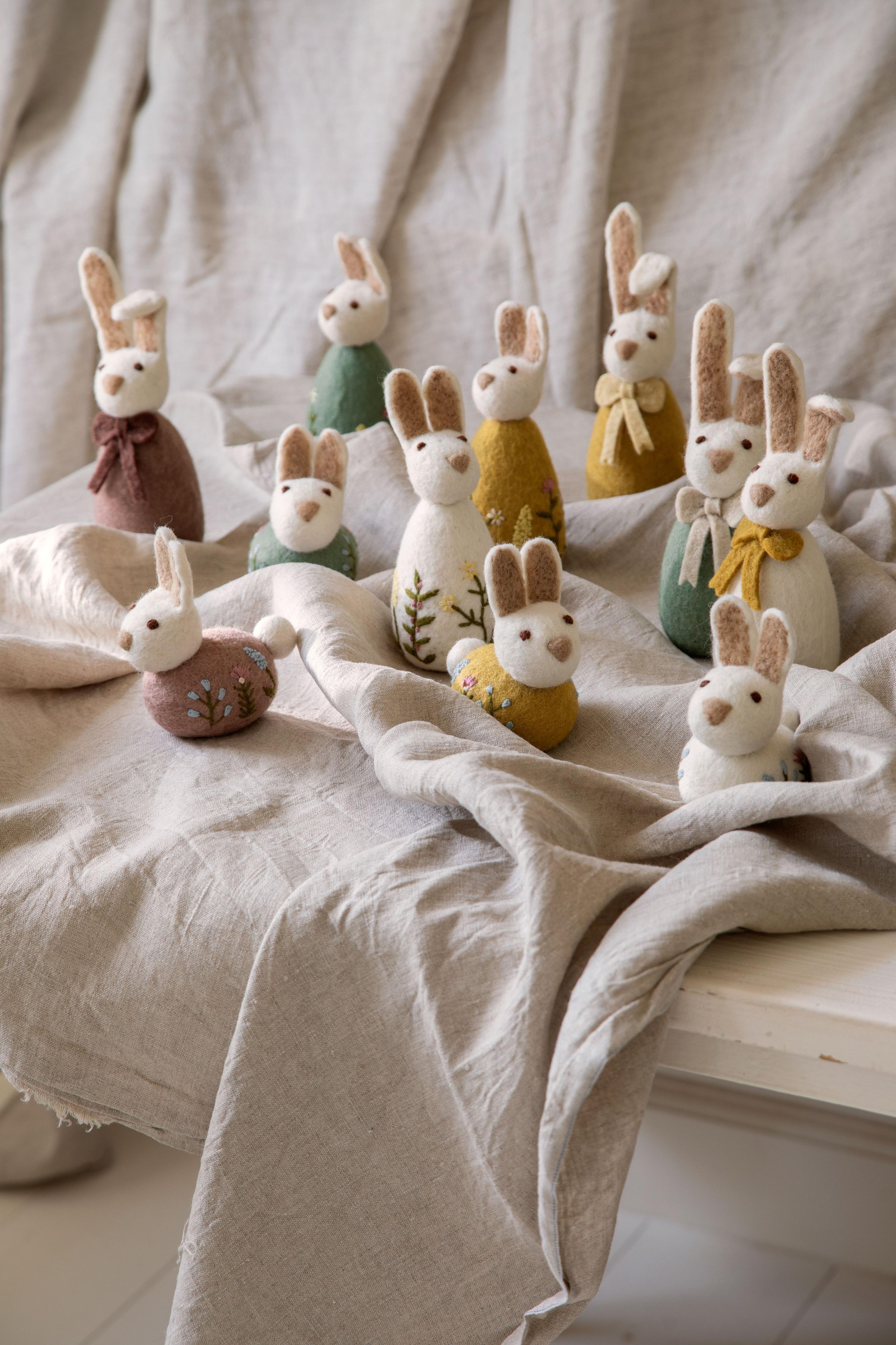 Felt bunny figures with colorful scarves and floral patterns on a beige cloth backdrop, arranged in a decorative display.