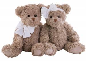 Two fluffy teddy bears with white bows sit side by side. The left bear has a neck bow, and the right bear has a head bow.