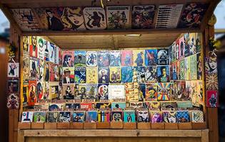 A wooden stall displaying a variety of colorful vintage-style posters and signs, featuring retro art, iconic figures, and music themes.
