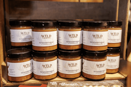 Stacked jars of Wild Viertel Hirschedelragout (venison ragout) with white labels and black lids on a wooden shelf.