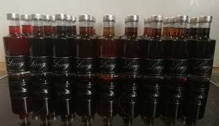 A row of various Lang liqueur bottles with black labels and silver caps, reflecting on a glossy surface.