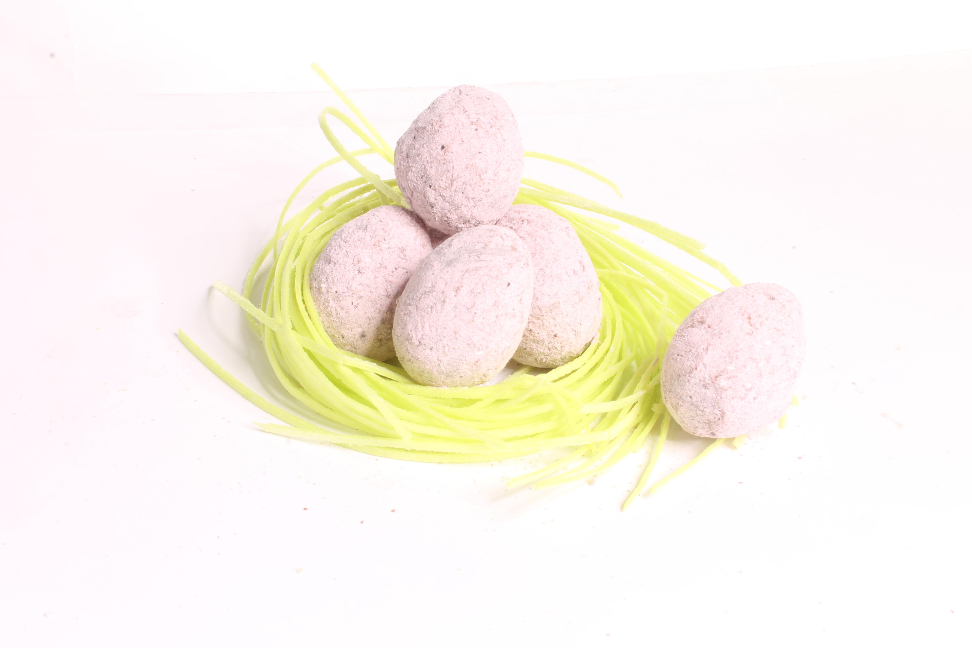 Five speckled eggs resting on a nest made of light green straw against a plain white background.