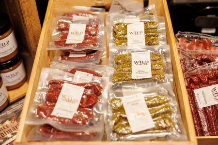 Vacuum-sealed cured sausages and herb-coated salami in a wooden display tray, labeled "WYLD Viertel".