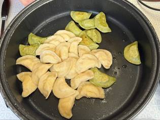A pan filled with cooked dumplings, some are green and others are beige, arranged on a stovetop.