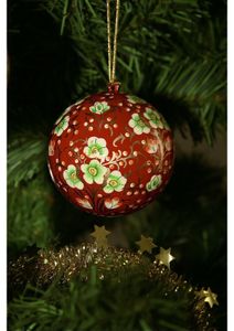 A red Christmas ornament with floral patterns hangs on a tree, adorned with green leaves and gold star-shaped tinsel below.