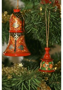 Two intricately painted red bell ornaments with floral and leaf designs hanging on a decorated Christmas tree.