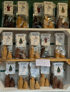 Shelves display packaged candles shaped like trees and figures, labeled "28 Lots." The scene conveys a festive, artisanal holiday ambiance.