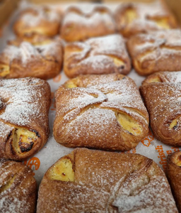 Freshly baked pastries topped with powdered sugar are arranged on a tray. The pastries have a golden-brown crust with visible folds, evoking warmth and comfort.