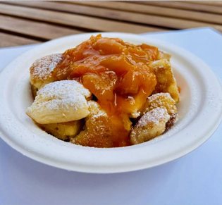 A bowl of powdered sugar-topped Kaiserschmarrn with apricot sauce on a wooden table.