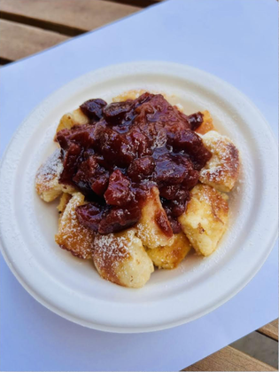 A plate of golden, fluffy Kaiserschmarrn topped with dark red plum compote, served on a white dish against a wooden background.