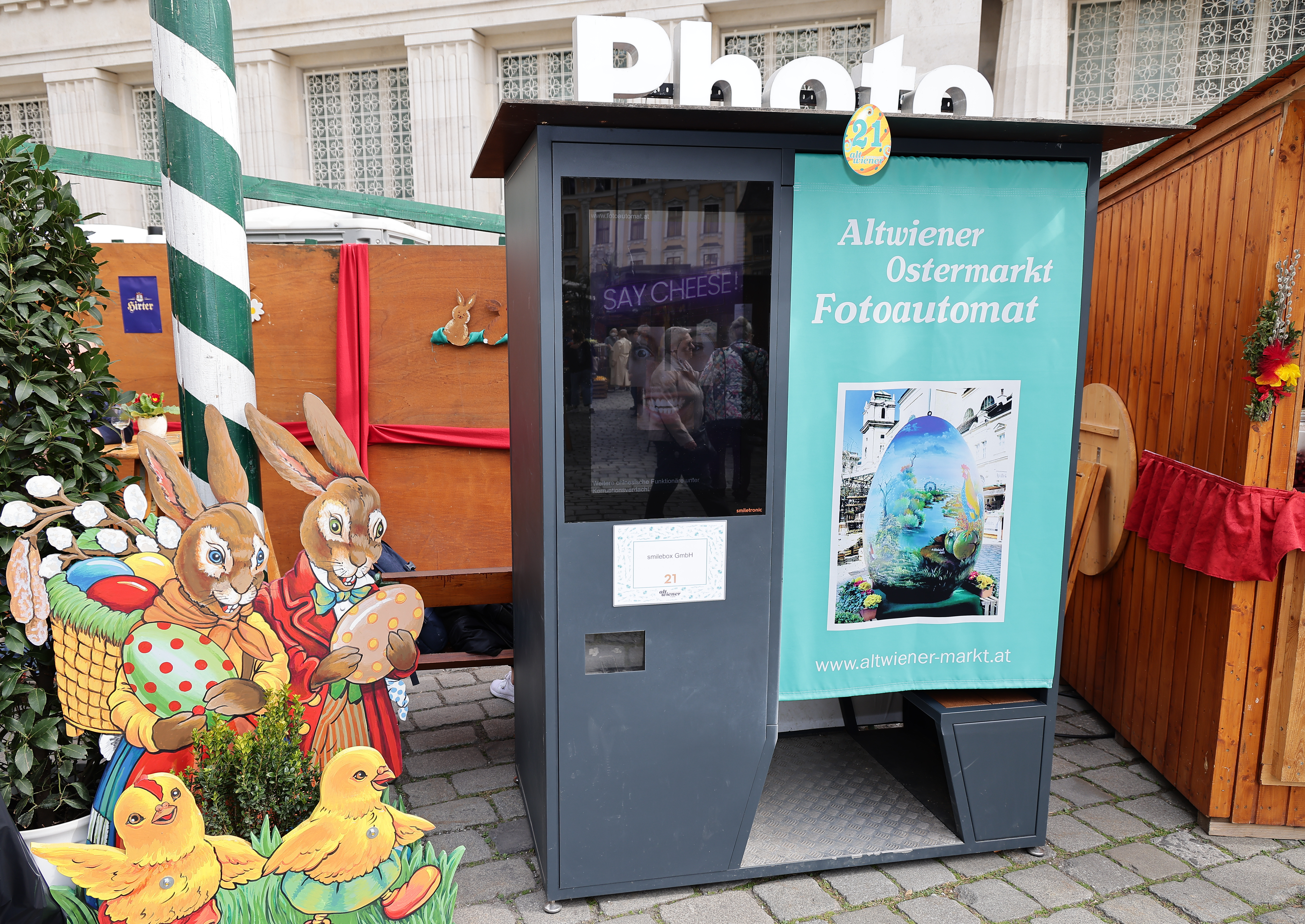 Photo booth at a market with Easter decorations, including a colorful poster and cardboard cutouts of rabbits carrying baskets.