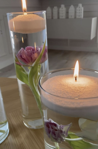 Lit floating candles in glass vases with submerged pink tulips, placed on a wooden surface, creating a serene ambiance.