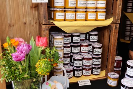 Jars of jam stacked on wooden shelves with a bouquet of colorful flowers in a vase nearby.