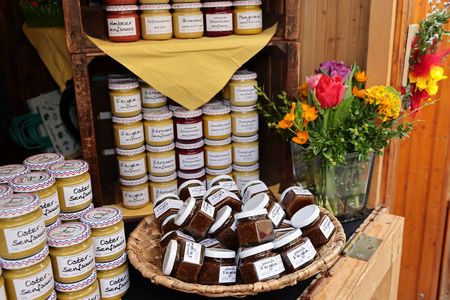 Jars of jam displayed on wooden shelves, with more jars in a basket. A vase of colorful flowers is placed nearby.