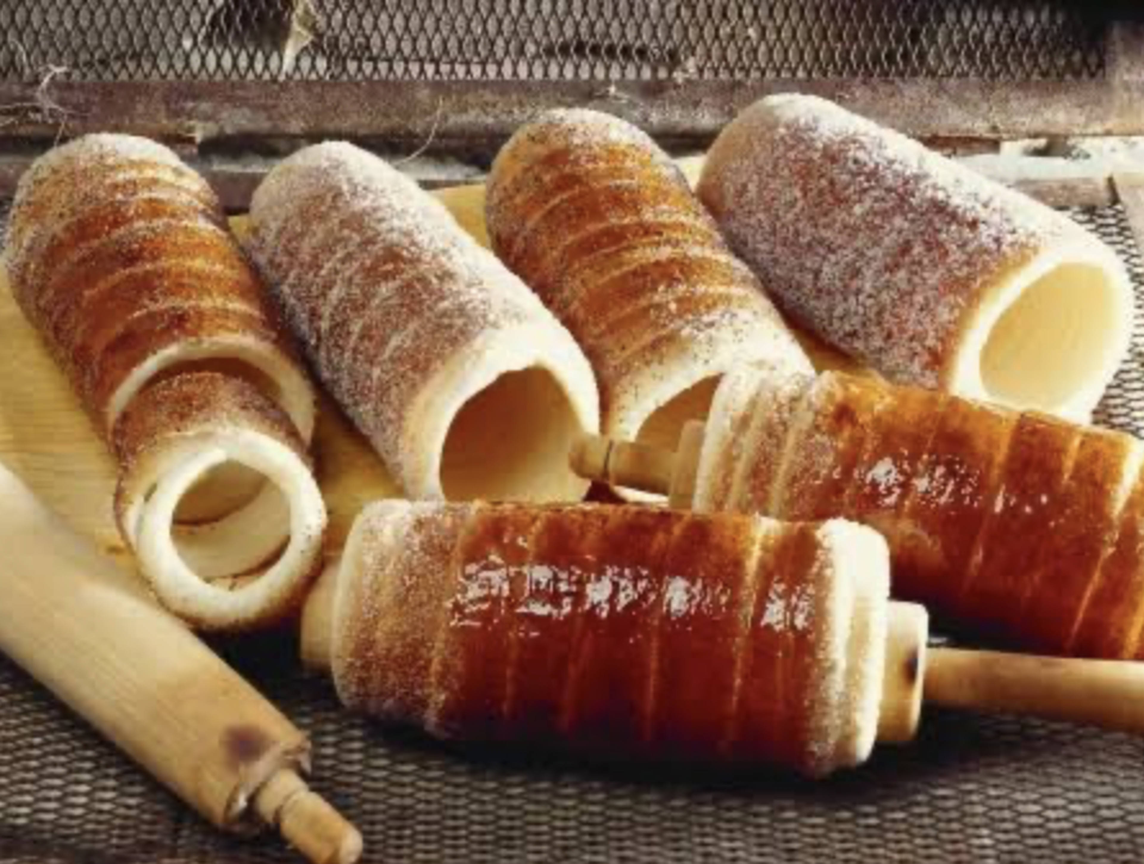 Several pieces of kürtőskalács, or chimney cakes, are displayed on a wooden board. They are golden-brown and coated with sugar.