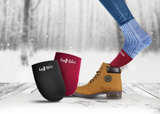 A person wearing blue socks and brown boots steps on a snowy wooden surface, with two insoles labeled "happy feet" nearby.