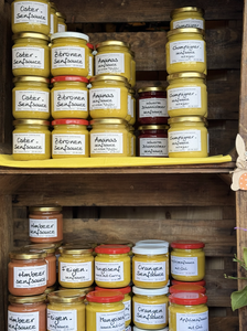 Jars of various homemade mustard sauces and spreads on shelves, labeled with flavors like lemon, pineapple, and fig.