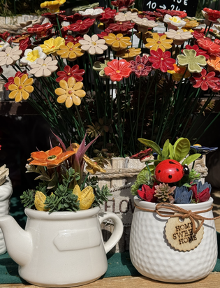 Ceramic pots with colorful flower arrangements; one pot is shaped like a teapot, the other has a "Home Sweet Home" tag with a ladybug decoration.
