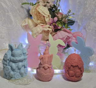 Colorful carved candles shaped like bunnies, eggs, and Easter designs in front of flowers and fairy lights.