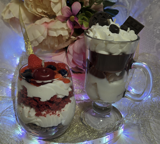 Two dessert cups with whipped cream, berries, and chocolate garnishes. One is paired with a second layer of chocolate in a clear glass mug.