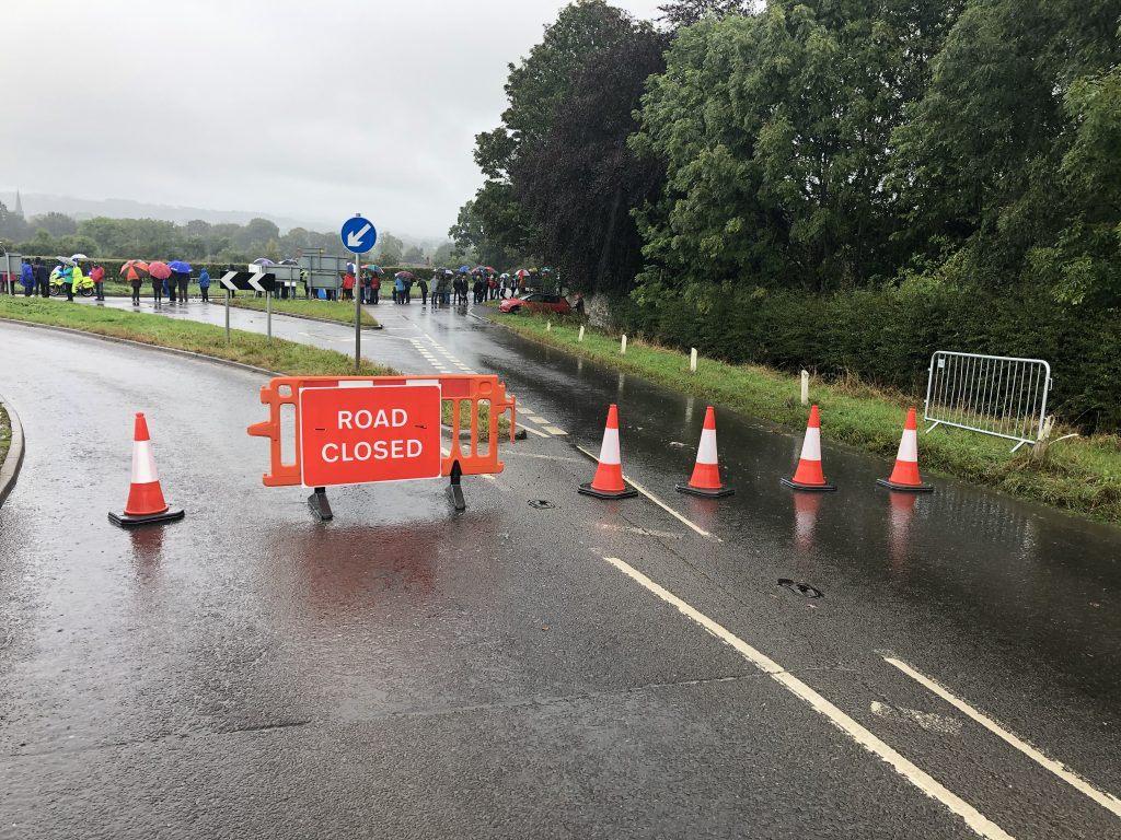 A road closed sign and spectators in the background