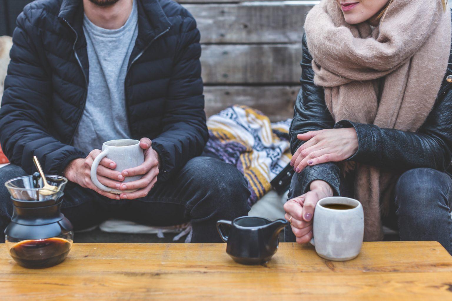 A couple in winter clothing, drinking coffee al fresco.