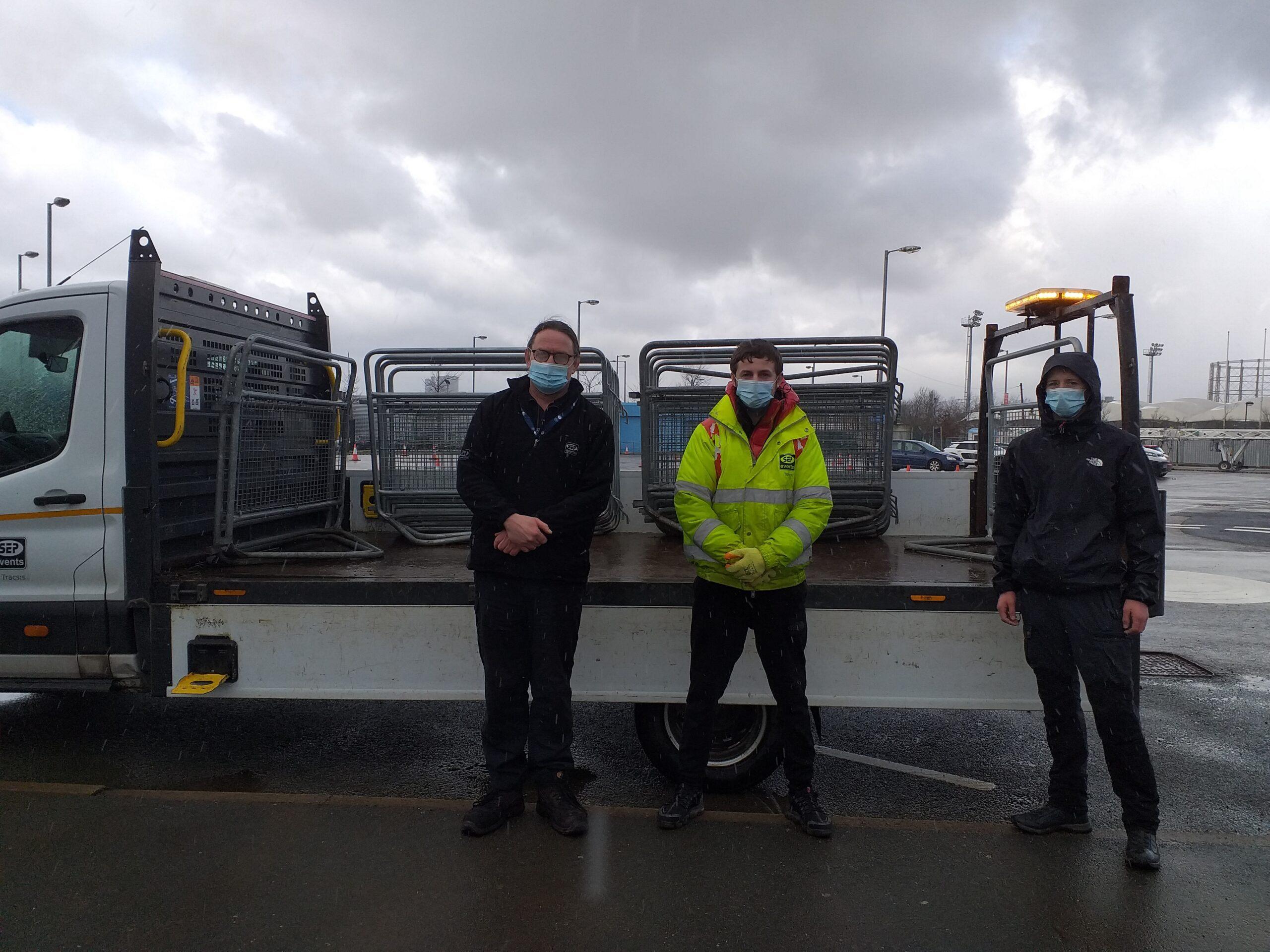 Three people standing in front of a flat-back lorry.