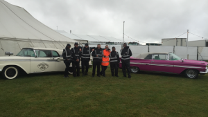 A group of marshals pose for a photo in front of two vintage cars