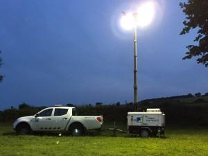 A vehicle towing a trailer under floodlights