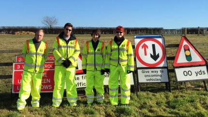 Four SEP team members in high visibility clothing posing for a photo in front of road signs