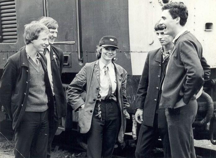 a group of men and a woman talking in front of a train