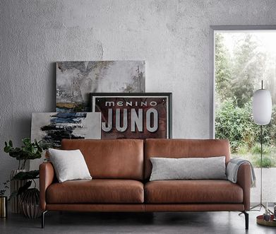 Braunes Ledersofa mit grauen Kissen vor Wand mit großen Bildern