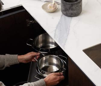 Topf wird in Küchenschrank verstaut. Mörser auf Arbeitsplatte.