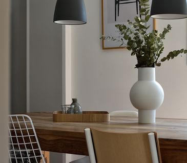 Massivholzesstisch im Esszimmer mit weißer Vase und grünen Pflanzen