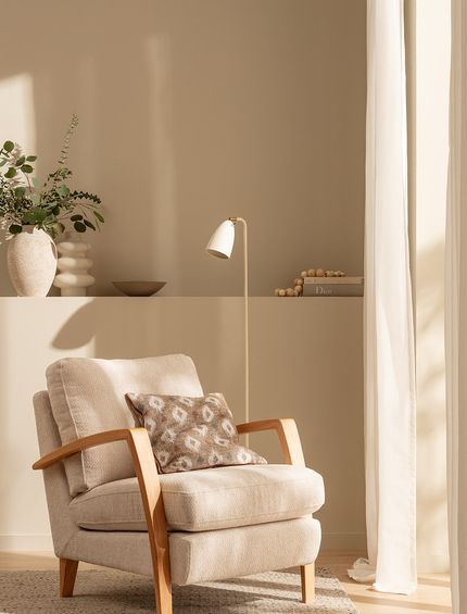 Beiger Sessel mit Holzarmlehnen in gemütlichem Wohnzimmer.