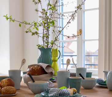 Esstisch frühlingshaft dekoriert mit buntem Geschirr und blühenden Zweigen.