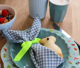 Buntes Geschirr mit Oster-Deko und Hefehasen auf einem Esstisch.