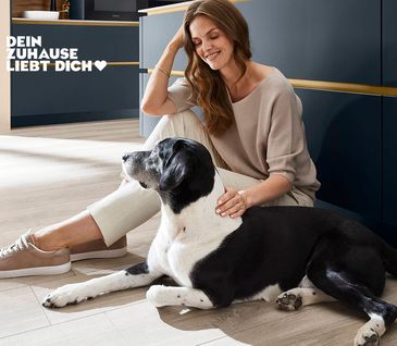 Frau sitzt entspannt mit ihrem Hund auf dem Boden ihrer Küche vor Kücheninsel in der Farbe Petrol.