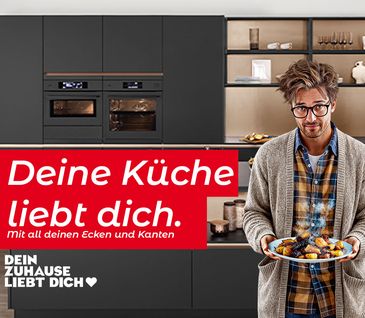 Junger Mann steht mit Teller in seiner neuen nobilia Küche in der Farbe Anthrazit.