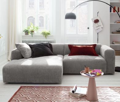 Zierlicher rosafarbener Beistelltisch mit bunten Zetteln und einer Tasse vor einem grauen Sofa.