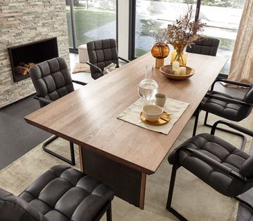 Dunkelgrau gesteppte Lederstühle an einem Massivholzesstisch der schön dekoriert ist.