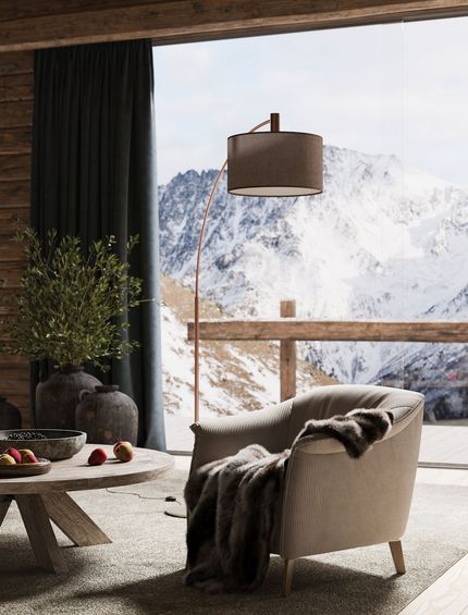 Beiger Sessel mit brauner Felldecke, rundem Beistelltisch und Stehlampe vor heller Fensterfront mit Bergblick.