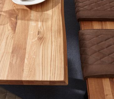 Tischplatte aus hochwertigem Massivholz neben Sitzbank aus Holz mit braunen Sitzpolster aus Leder