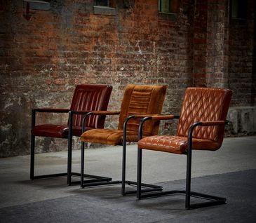 Drei moderne, cognacfarbene Lederstühle vor Ziegelwand.