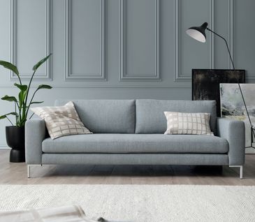 Hellblaues Sofa vor hellblauer Wand und bunten Bildern, die am Boden lehnen.